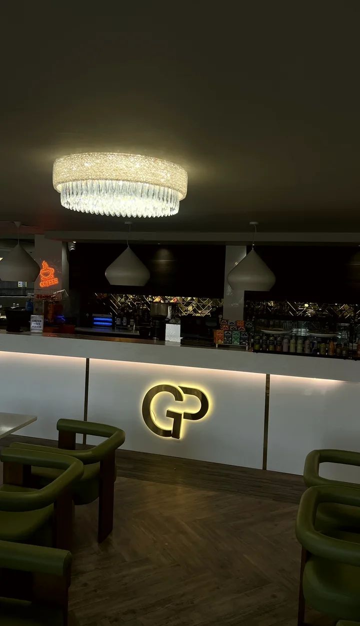 The coffee bar under a crystal chandelier, with a glowing GP logo and green armchairs