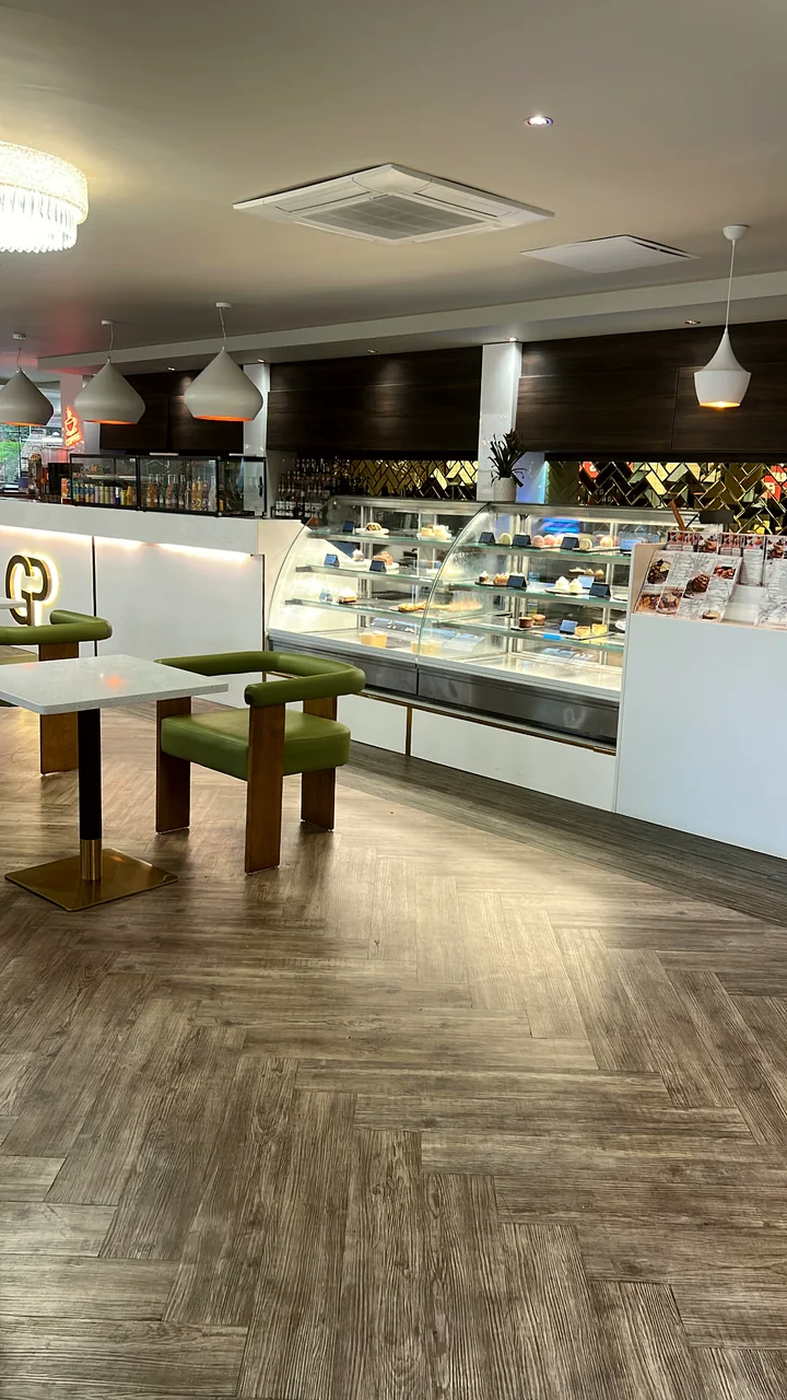 The coffee shop counter lined with cakes and pastries, with green leather armchairs